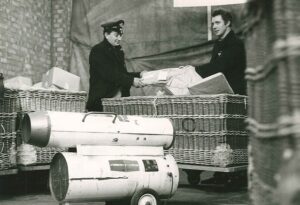 Historical black-and-white photo of two men handling heating equipment next to large industrial heaters, representing the early days of Andrews Heat for Hire